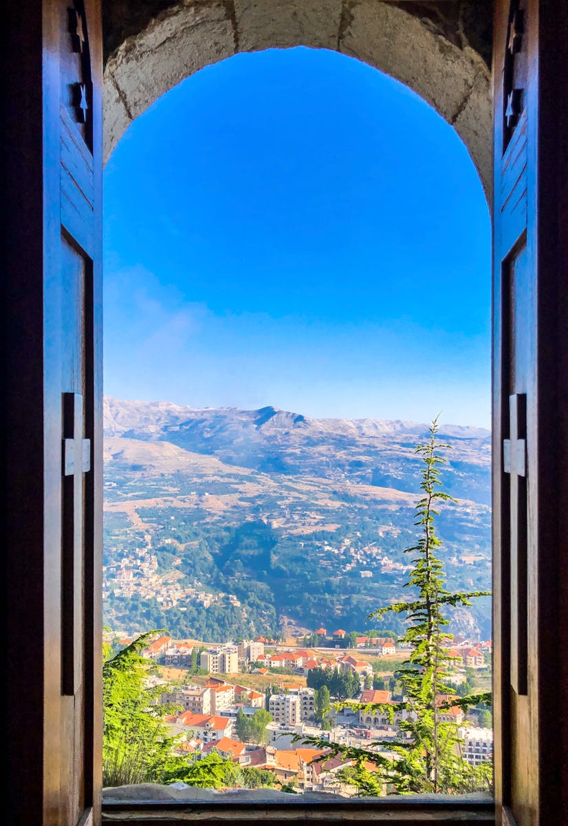 Picturesque view of Ehden, Lebanon through a wooden window frame with mountains and clear blue sky.